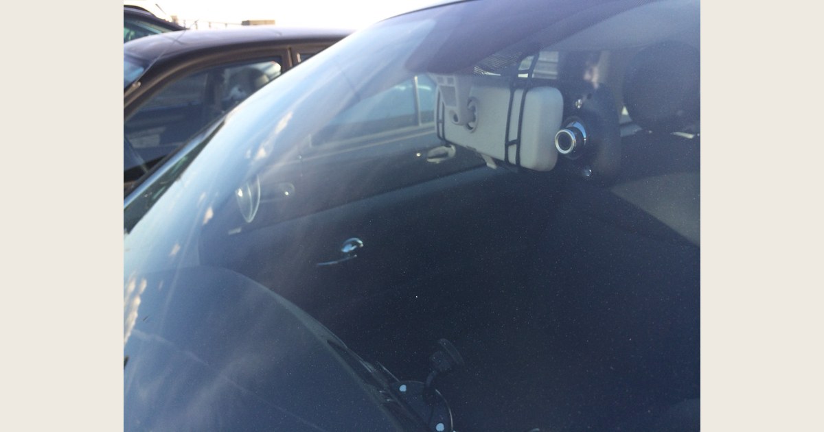 Exterior view through the windshield of a car, showing a rearview-mirror-mounted dash cam
