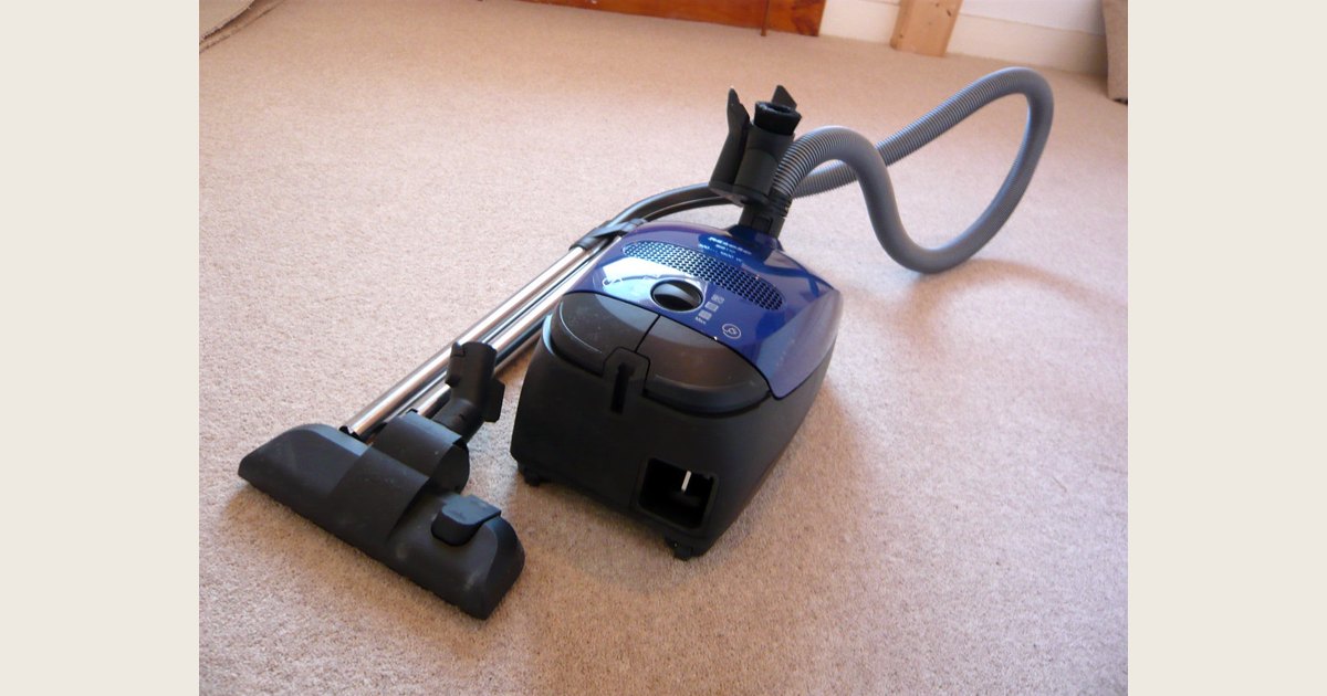 A canister vacuum with a long flexible hose, metal extension tube, and floor nozzle.